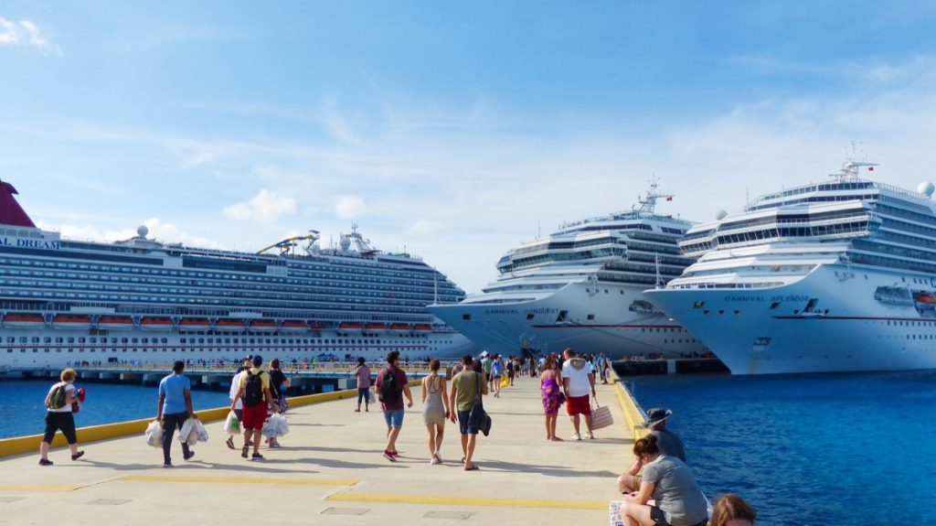 people walking on the pier with three cruise ships in the background