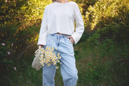 woman standing outside with a bouquet of daisies in an eco friendly net bag. she's wearing light jeans and a white top