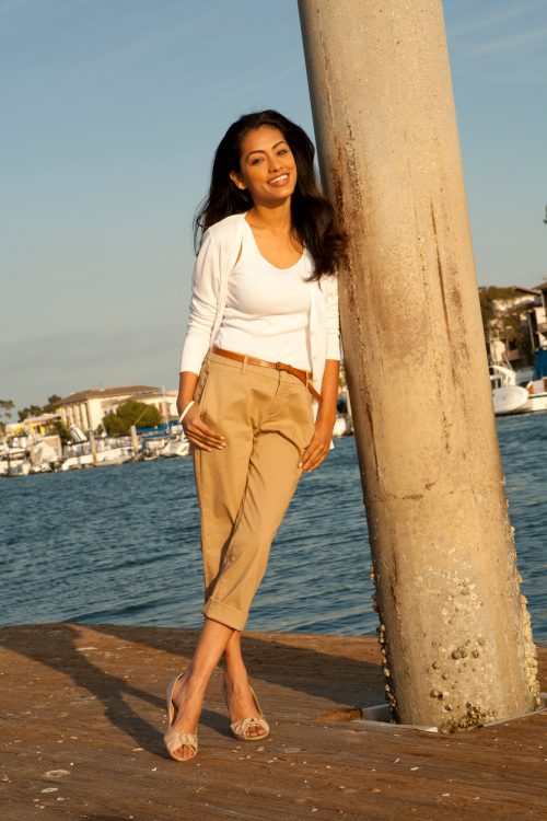 woman wearing capri pants and neutral colors, leaning against a pole at the shore