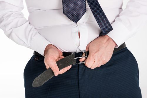 partial view of overweight man in formal wear putting on tight pants isolated on white