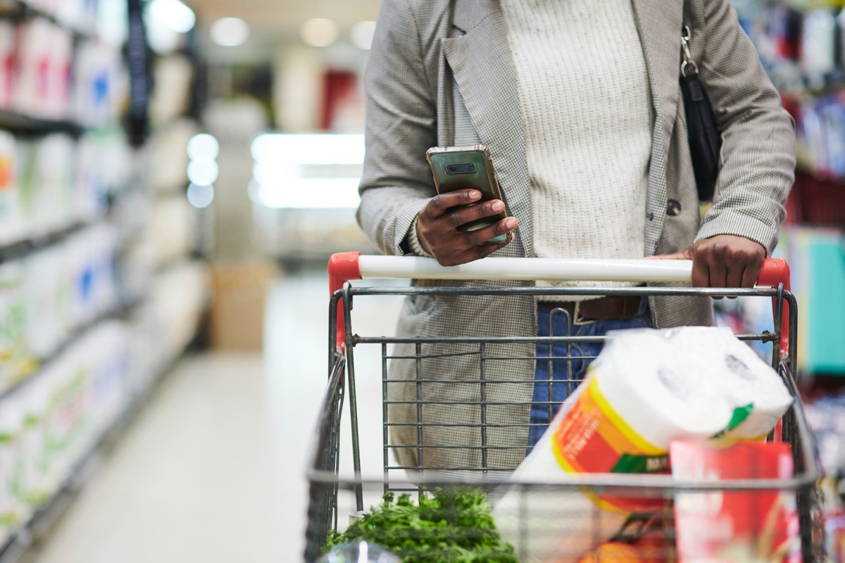 woman, hands and phone with trolley for shopping, checklist or ecommerce at the mall.