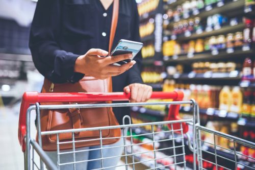 Cropped shot of a woman using a smartphone while shopping in a grocery store