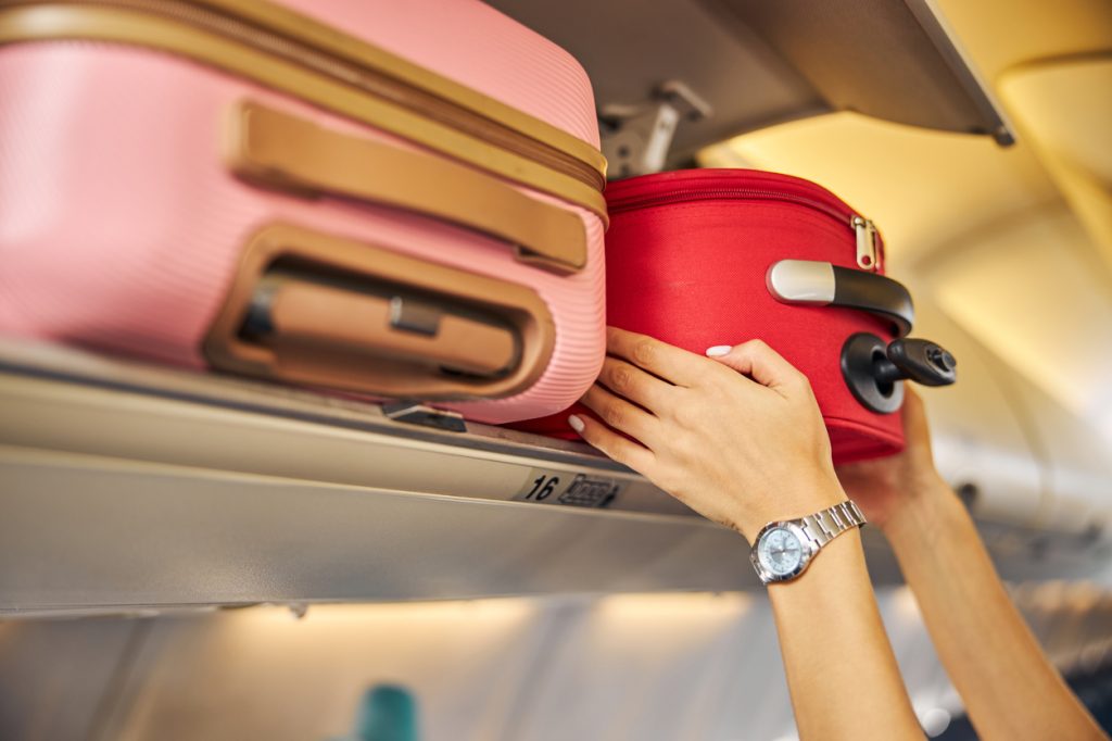 Person putting carry-on bag in overhead compartment.