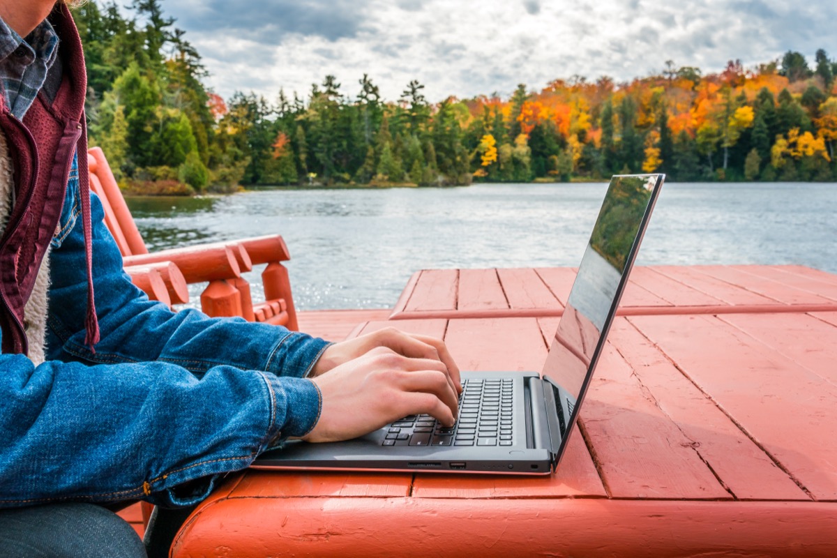 Work from anywhere - working on laptop beneath the autumn sky while on a deck near the water's edge. concept - background