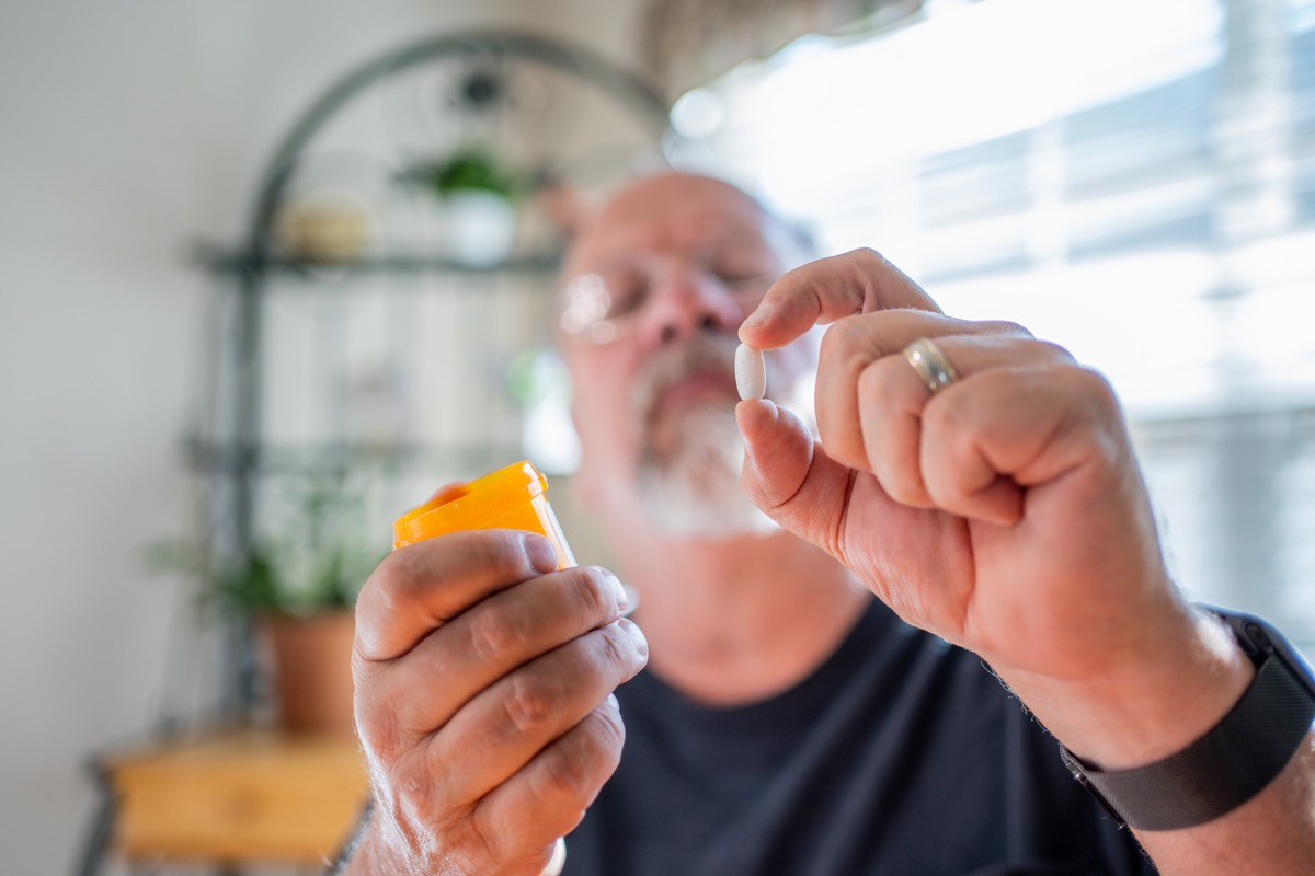 Mature Man Scrutinizing His Perscription Medications Holding a Pill in One Hand and the Bottle in the Other In a Modern Home