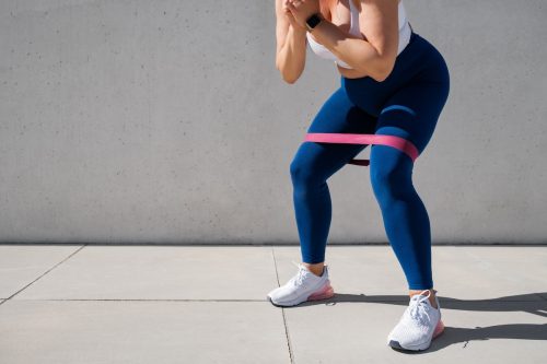 Woman in blue leggings exercising outdoors with resistance band around thighs