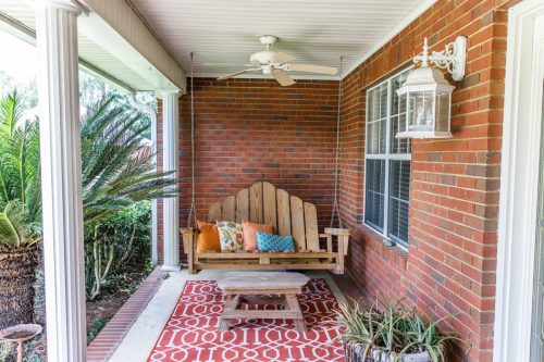 Colorful and modern bohemian boho outdoor front porch decoration with seating and a plant. The house is red brick and traditional.