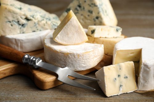 Different sorts of cheese and fork on wooden table, closeup