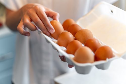 women with holding a cardboard egg box full of her eggs. the girl takes one chicken egg from a white box