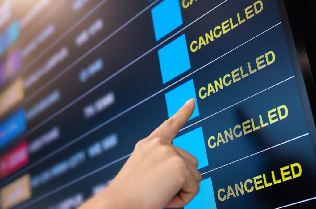 Finger pointing at cancelled notice on flight departures board