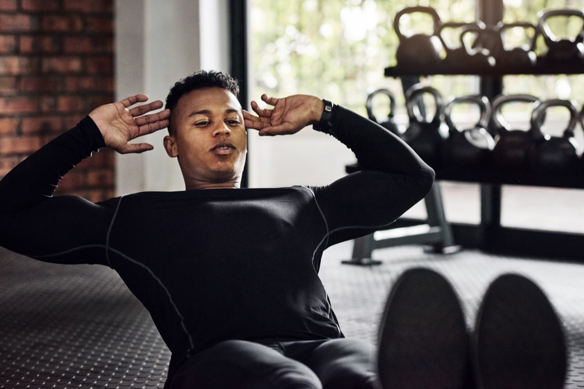 Shot of a young man doing sit ups at the gym