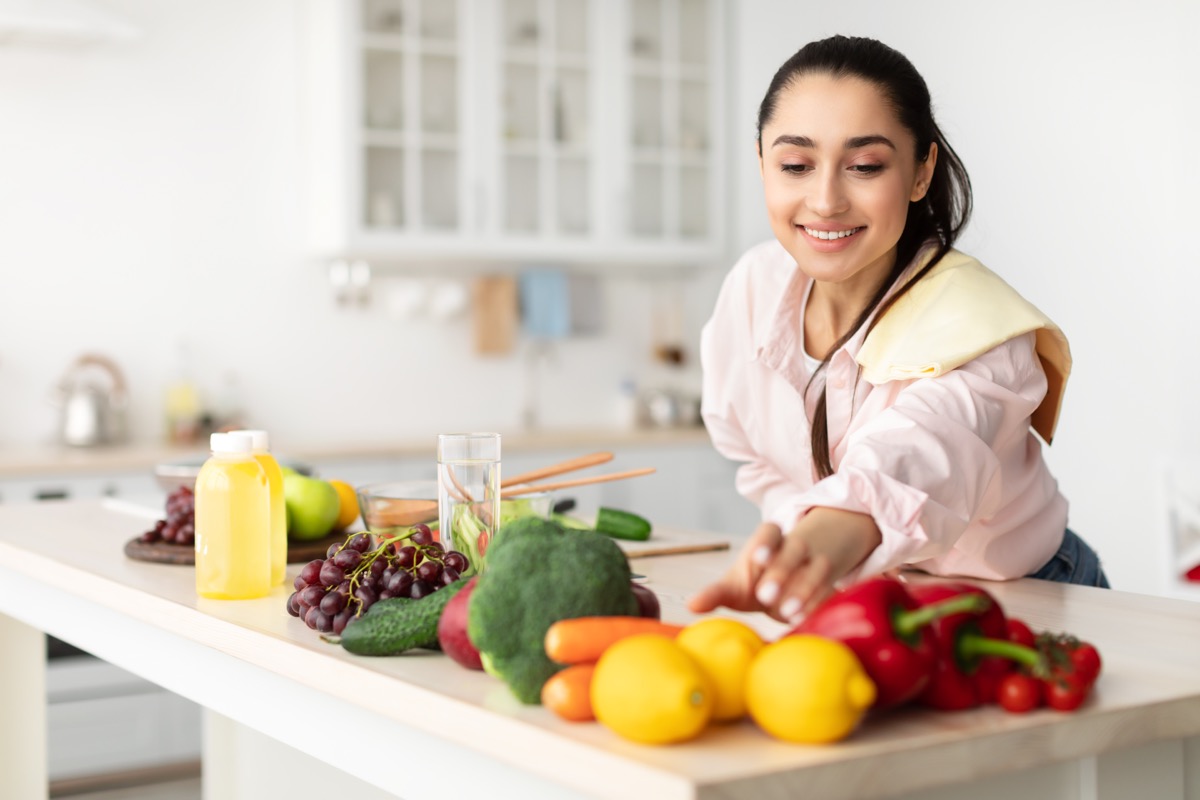 young woman cooking fresh organic salad at home in modern kitchen, reaching for vegetables