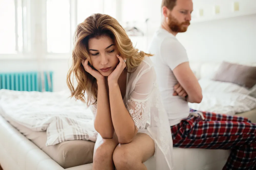 A young couple mad at one another while sitting on their bed