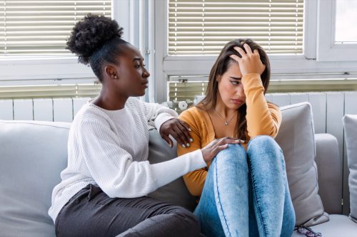 Woman comforting another woman as they sit on a couch together