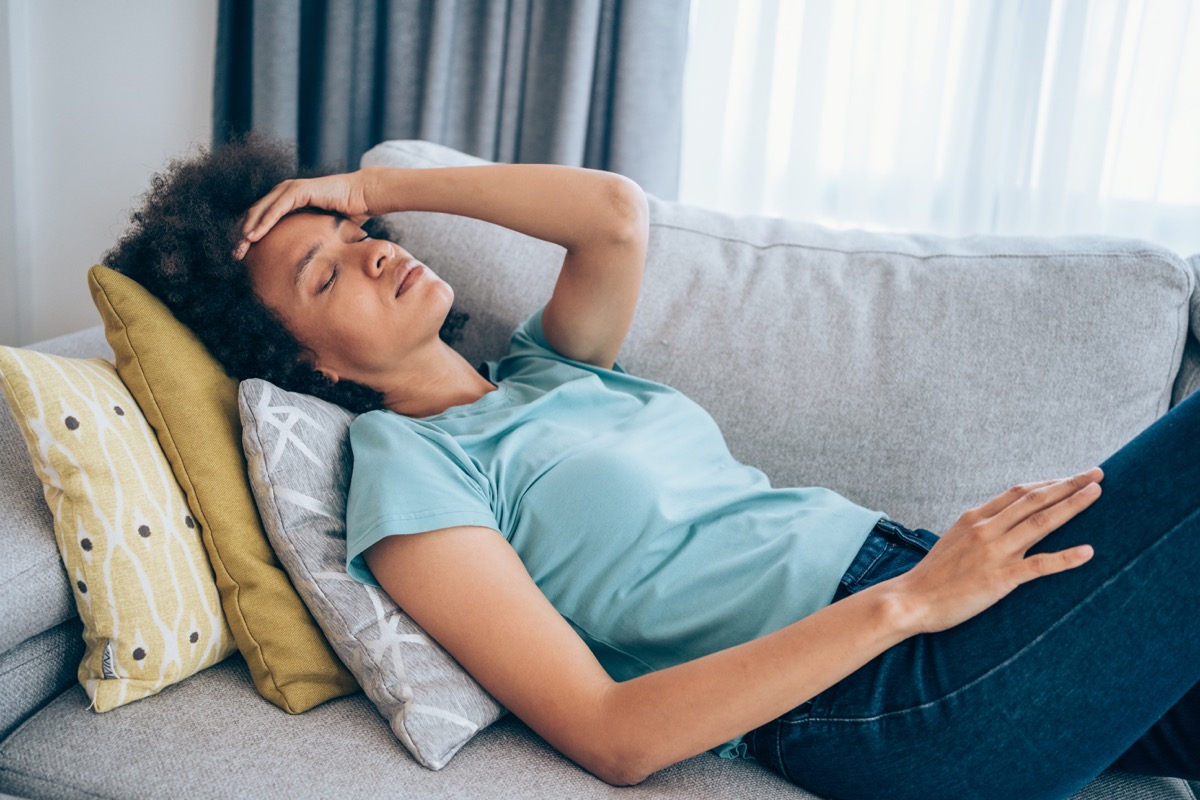 Sick young woman lying on the couch and holding her head with hand. Ill woman lying on the sofa with high temperature.