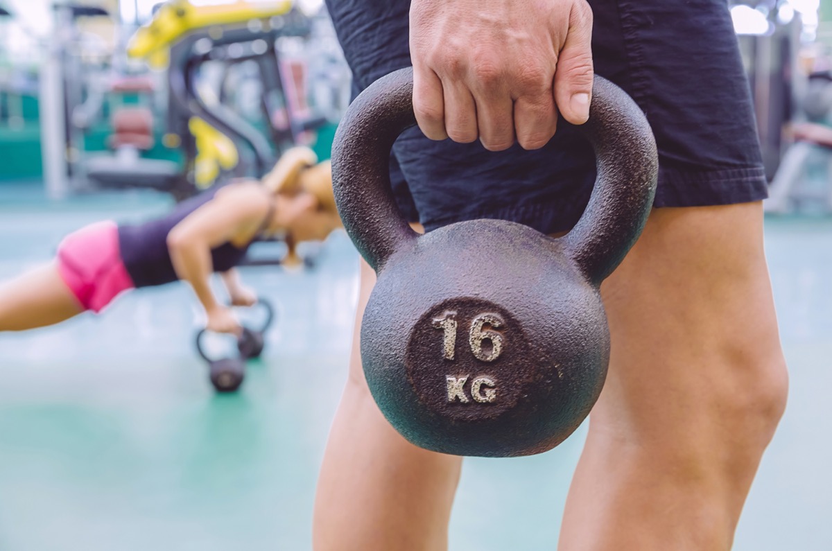 Closeup of athletic man holding black iron kettlebell and woman doing pushups over kettlebells in training