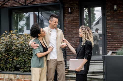 Realtor giving house key to a happy couple outside of a home