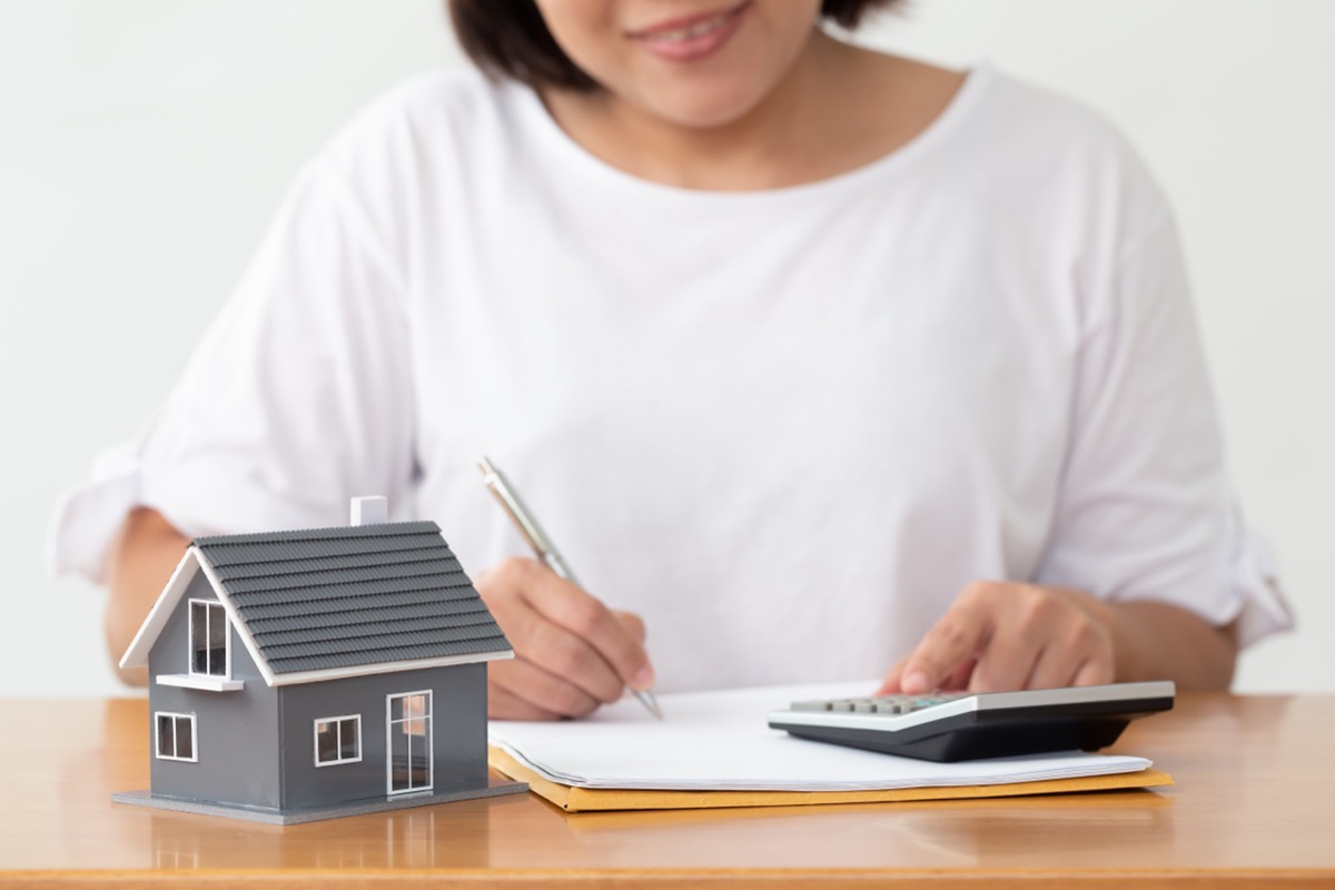 woman using a calculator with a model of a house on the desk to explain the concept of refinancing a mortgage