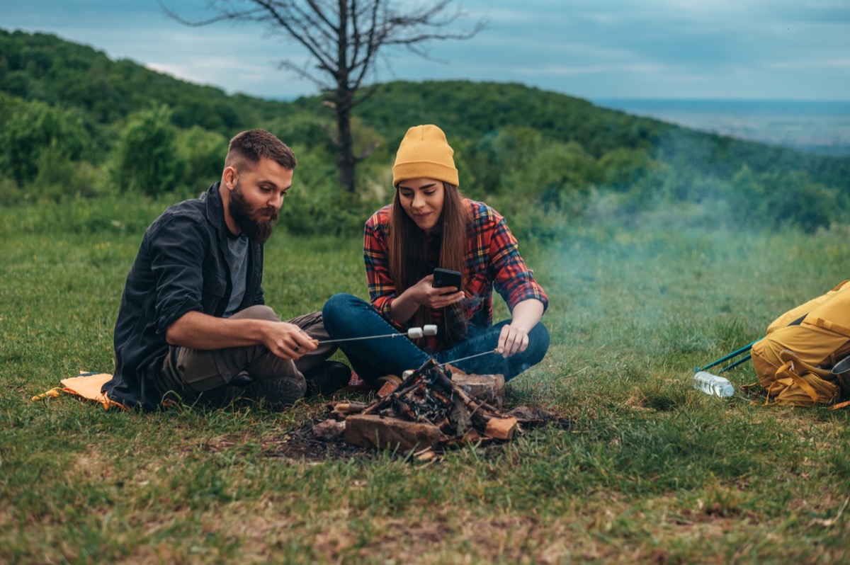 Couple of campers eating marshmallows while sitting near the camp fire while camping in the nature