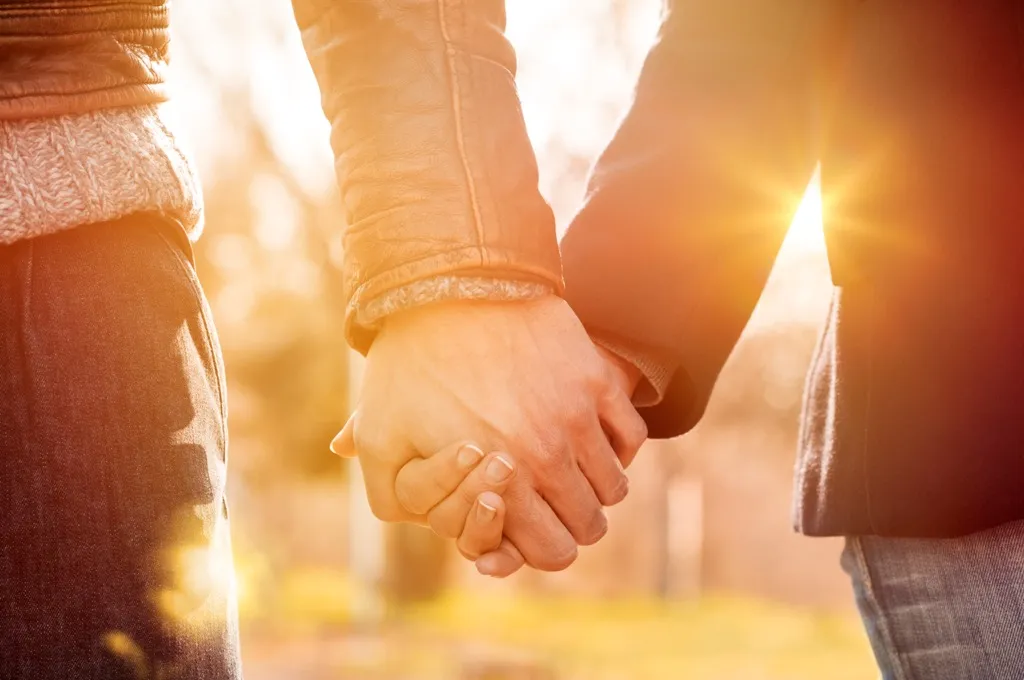 closeup of a couple holding hands outside during sunset