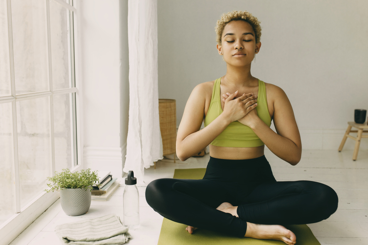 Young woman racticing yoga at home in black leggings sitting on floor i