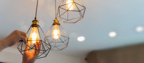 An electrician is installing spotlights on the ceiling. Handyman choosing between energy save and cheap incandescent lamp while changing light in the appartment