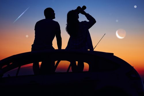 A couple sitting on the roof of a car with binoculars and watching the night sky and shooting stars