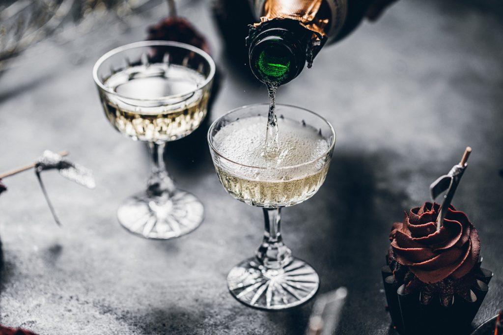 Close-up of pouring champagne in a glasses over black table with cupcake