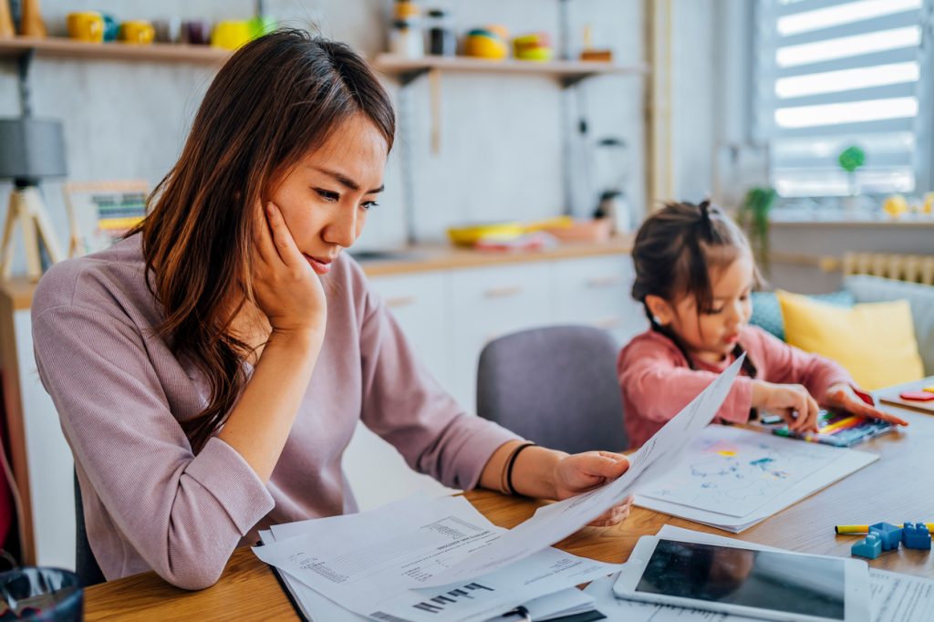 A woman looking anxiously at financial records while sitting next to a young girl