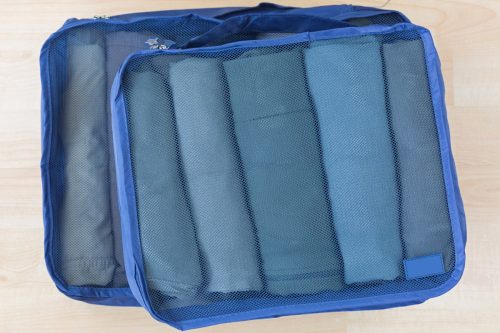 Cube meshed bags with rolled clothes, t-shirt, pants. Set of travel organizer to help packing luggage easy, well organized