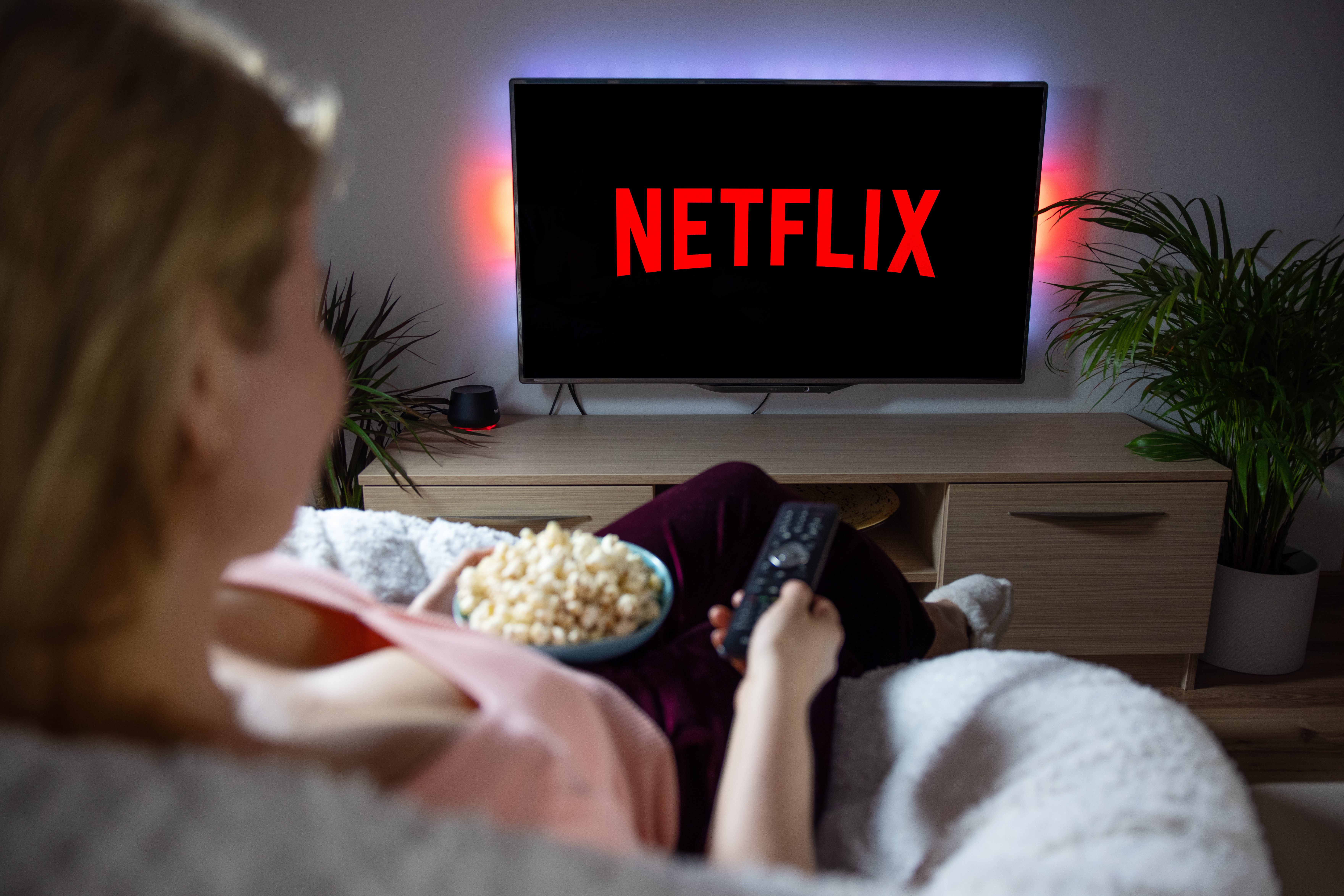 Một người phụ nữ đang ngồi trên ghế dài với bỏng ngô và xem Netflix trên TV