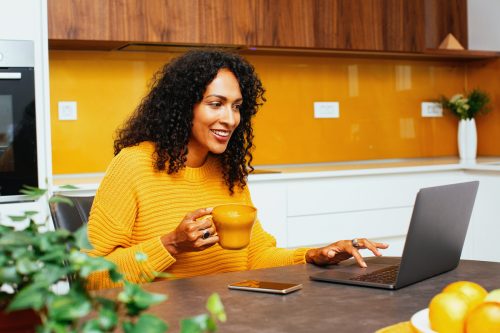 Young woman in yellow sweater smiling while looking at her computer