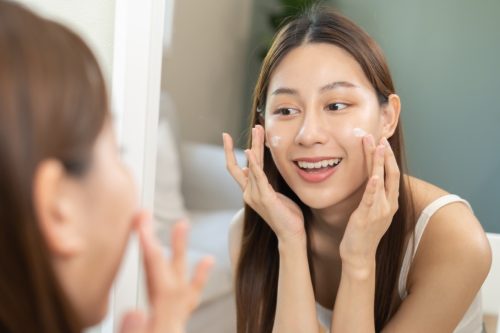 người phụ nữ trẻ mỉm cười đang thoa kem dưỡng ẩm cho quy trình chăm sóc da