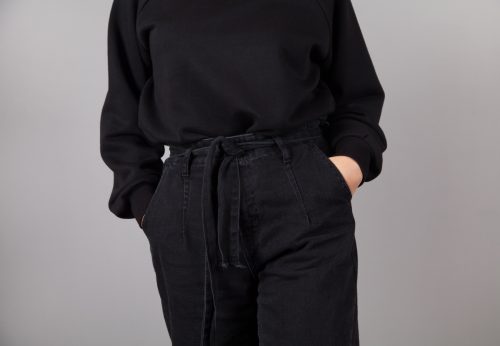 Cropped image of a woman wearing a black sweater and black jeans against a gray background