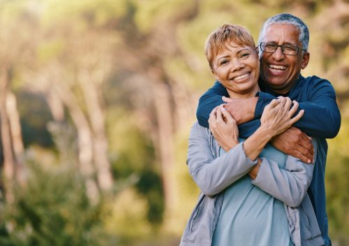 Happy Middle Aged Couple hugging outdoors with trees in the background