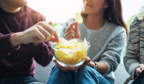 Closeup image of friends sharing and eating potato chips