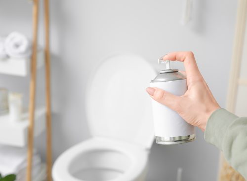 Woman spraying air freshener in bathroom