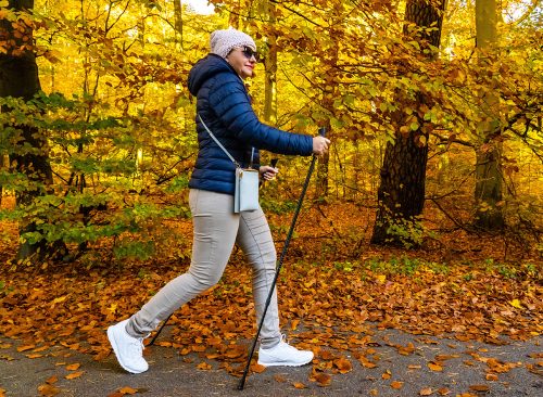 Autumnal Nordic walking - mid-adult beautiful woman exercising in city park using Nordic walking poles