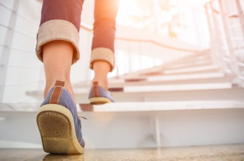 Young adult woman walking up the stairs with sun sport background.