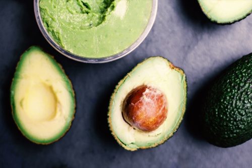 avocado cut into two halves near bowl of guacamole on black surface