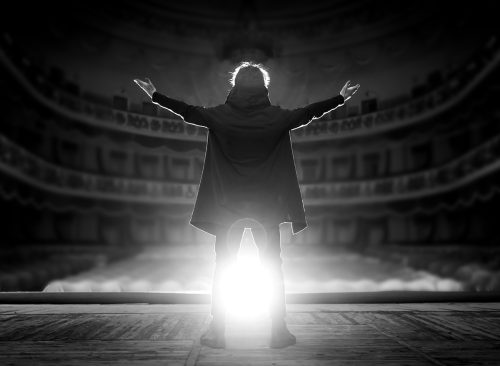 Professional male actor on the stage of the theater against the backdrop of an empty hall. Black and white photo