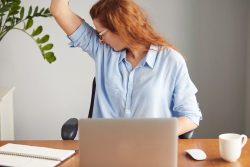 Portrait of a young woman wearing blue shirt smelling her armpit in an office