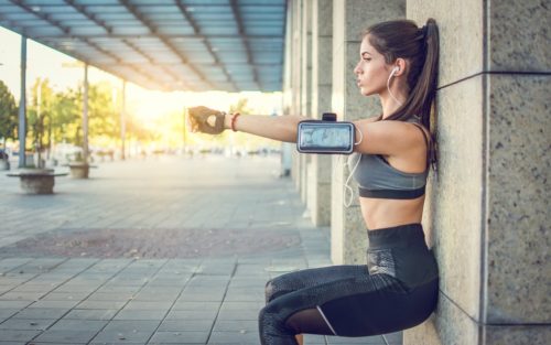 Young sportswoman doing squats against wall outdoors.