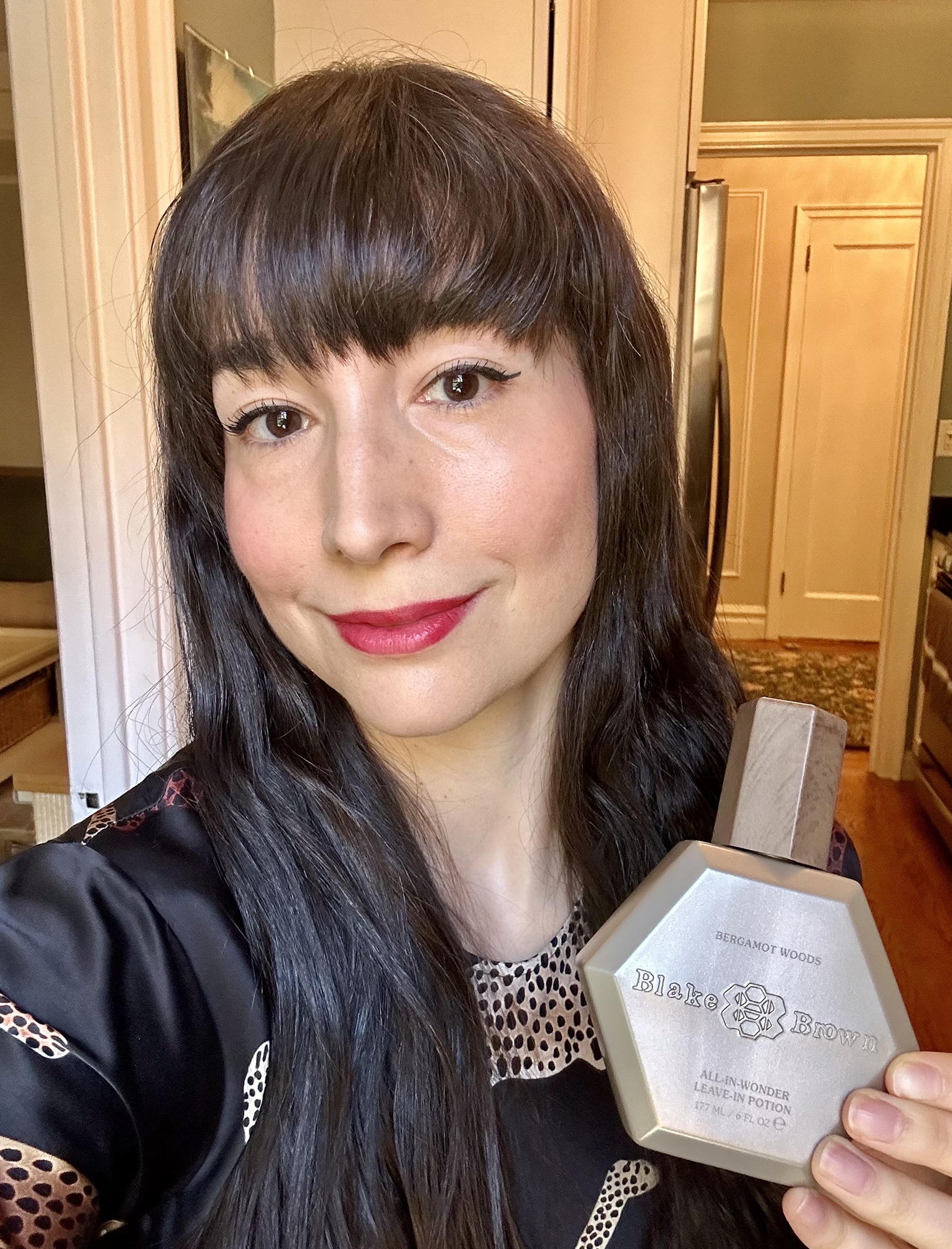 Elana Fishman holding a bottle of Blake Brown Bergamot Woods All-In-Wonder Leave-In Potion