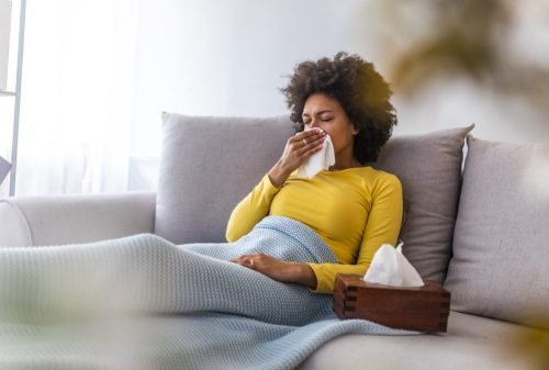 A woman blowing her nose while sick on the couch